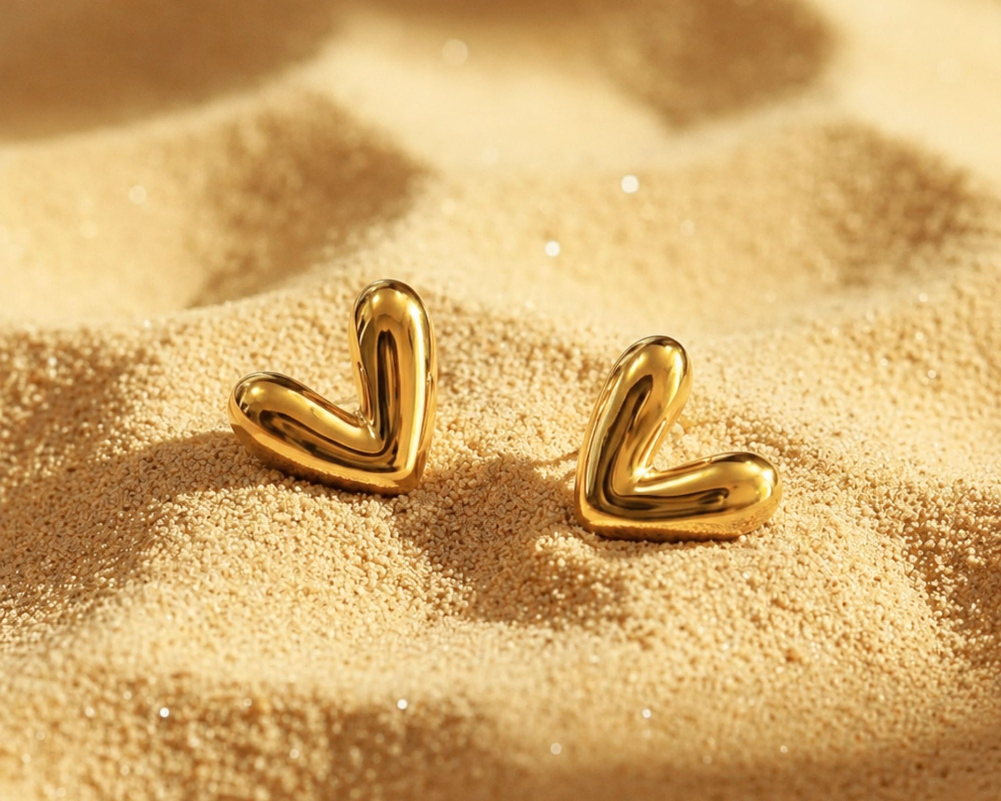 Salve Coquette gold-toned heart earrings with delicate heart-shaped design and shiny finish, displayed on a white background.