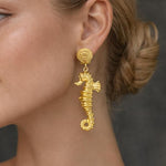 Gold sea horse drop dangle earrings by SALVE featuring intricate sea horse designs and elegant dangling style.