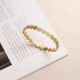 Salve Coquette floral daisy golden bracelet featuring delicate daisy charms and a shiny gold finish on a jewelry display.