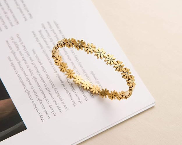 Salve Coquette floral daisy golden bracelet featuring delicate daisy charms and a shiny gold finish on a jewelry display.